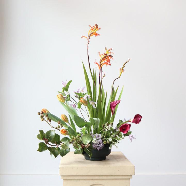 Spring Fountain | A floral arrangement made with blooms such as tulips, calla lilies, carnations and an assortment of other spring flowers. The colors are green, orange, magenta, and lilac.