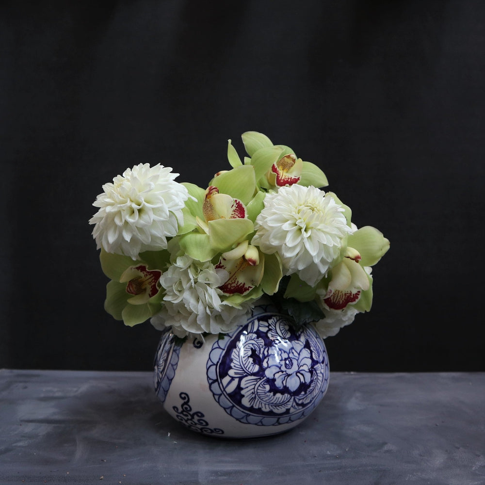 Floral arrangement in a blue patterned vase with 2 dahlias, green orchids and hydrangea. on a dark background. 