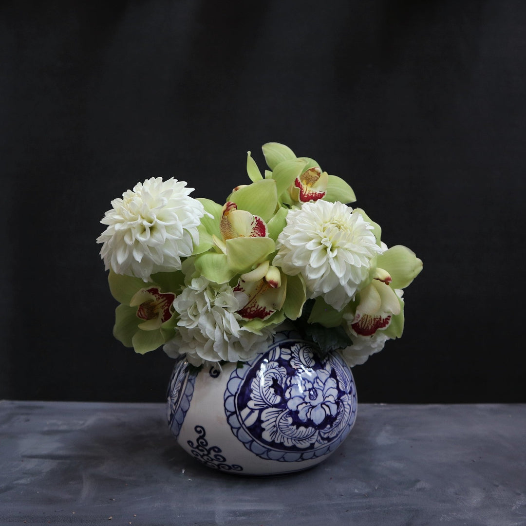 Floral arrangement in a blue patterned vase with 2 dahlias, green orchids and hydrangea. on a dark background. 