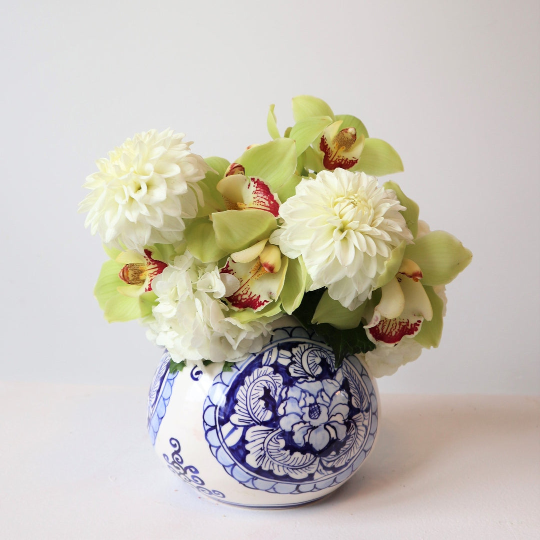 Floral arrangement in a blue patterned vase with 2 dahlias, green orchids and hydrangea. 