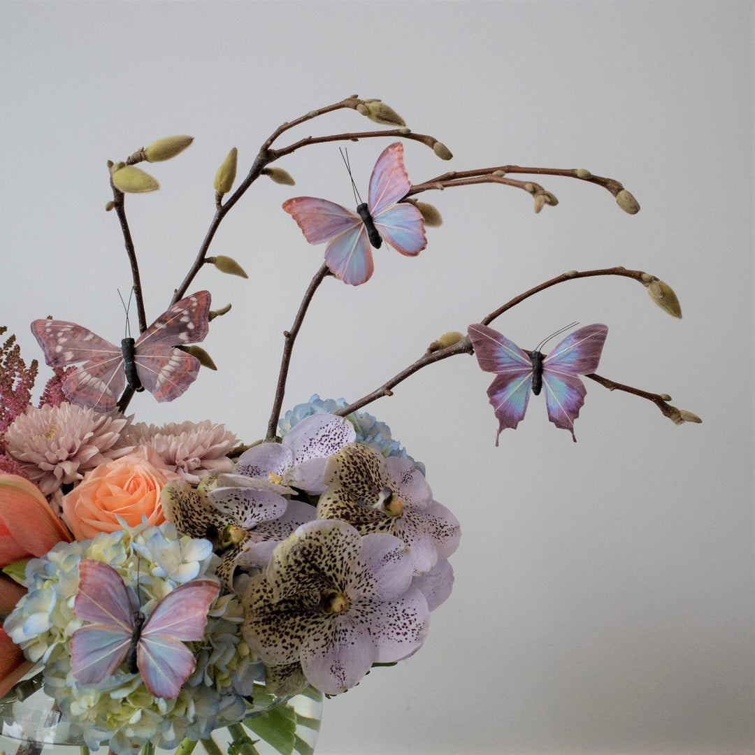 Whymsical floral arrangment with butterflies. Transparent bowl vase with Orchids, blue hydrangea, and decorative butterflies. Close up on pink astilbe.