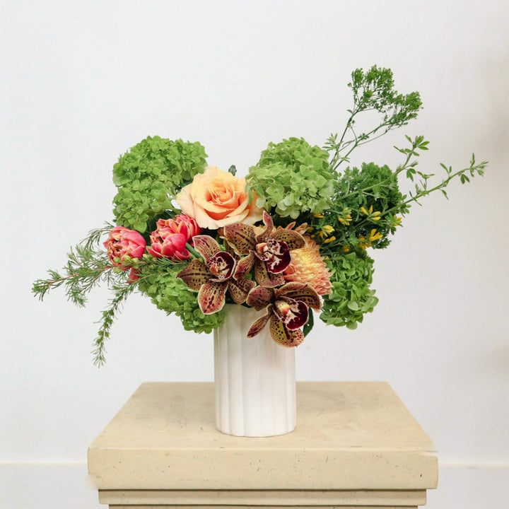 Delightful | A spring arrangement with double tulips, roses, orchids, green hydrangea, and other greenery. Vase is a white with slight ribbing. 