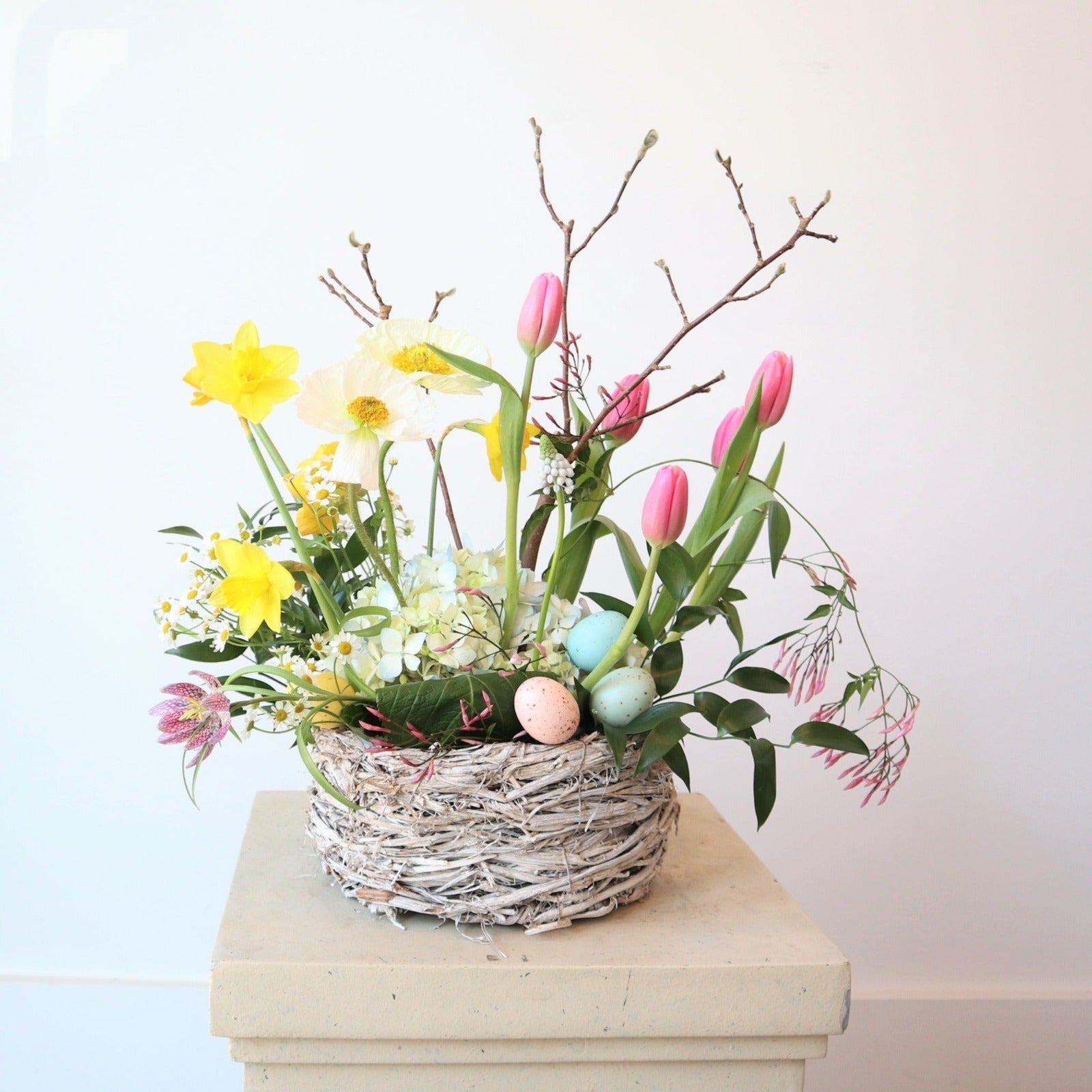 Easter Basket | A spring Easter arrangement with  yellow, white, pink, green, and accent branches. The arrangement is in a basket with decorative pink and blue eggs.