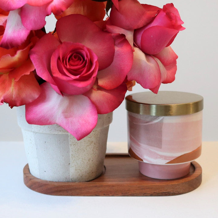 Close up of pink roses, vase, wooden base, and pink candle with gold lid.