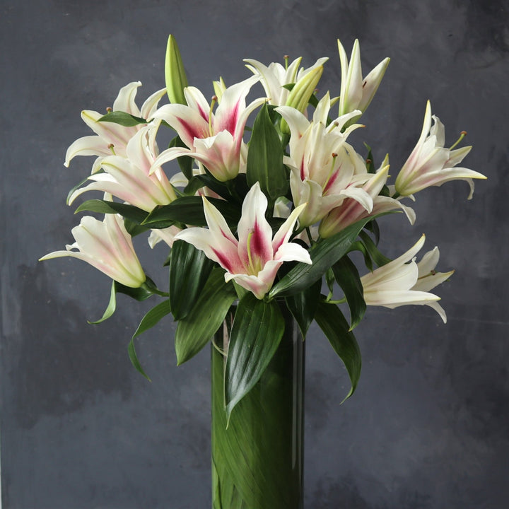Lilies in a clear vase with leaves on the inside wrapping around the stems of the flowers.