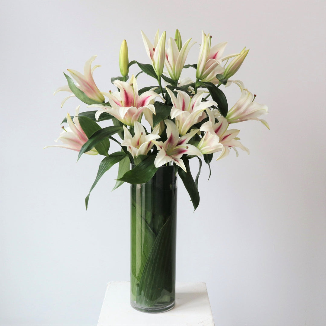 Lilies in a clear vase with leaves on the inside wrapping around the stems of the flowers.