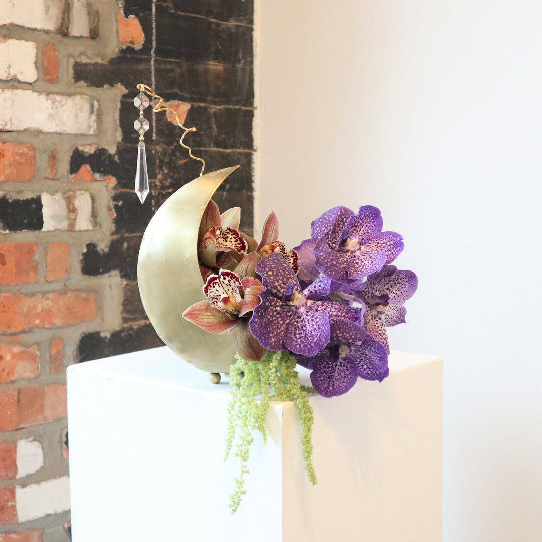 Arrangement with purple and red orchids with green ameranthus in a gold cresent shaped moon planter.