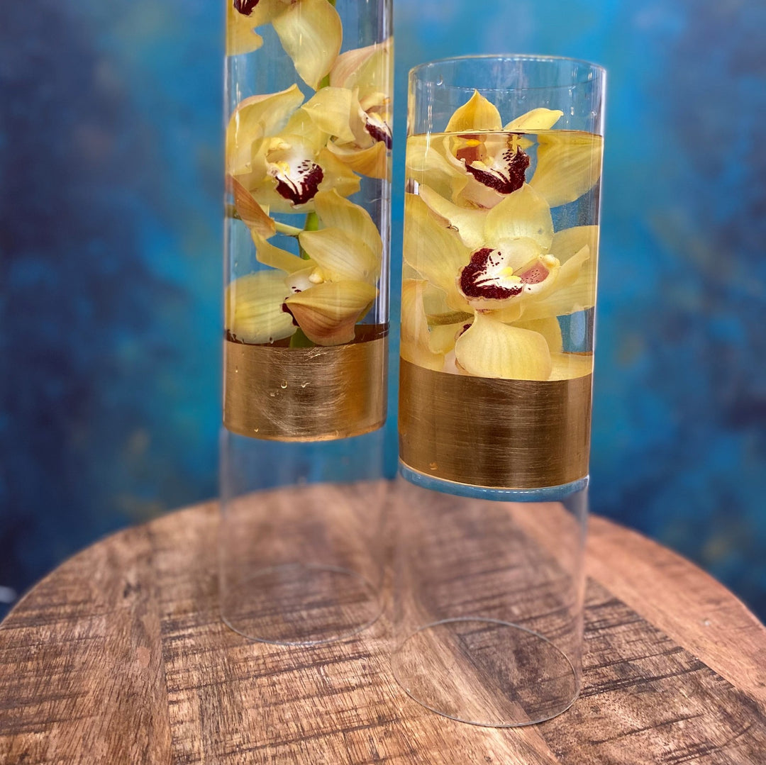Yellow Cymbidium orchids in clear vase with gold band.