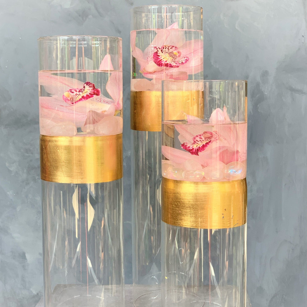 Orchid Trio Set | Pink orchids suspended in water with transparent rocks/crystals. The vase is transparent with a gold band across the middle.