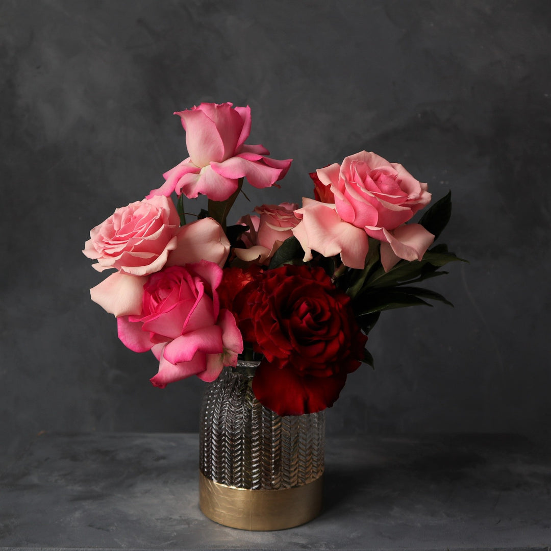 A variety of pink roses in different shades of pink, designed in a glass vase with gold bottom.