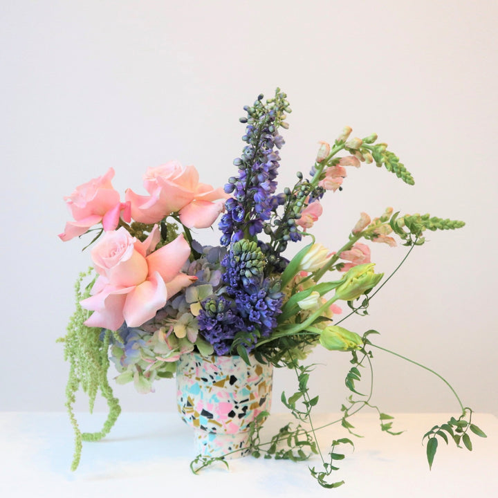 Shimmer: A spring arrangement with pink roses, purple/pink snapdragons, multi color hydrangea, ameranthus, and assorted greens. This arrangement is pictured in a blue, pink, white, and gold vase.