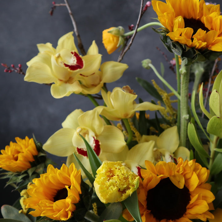 Yellow orchids in the center, accented by yellow sunflowers, tulips and branching.