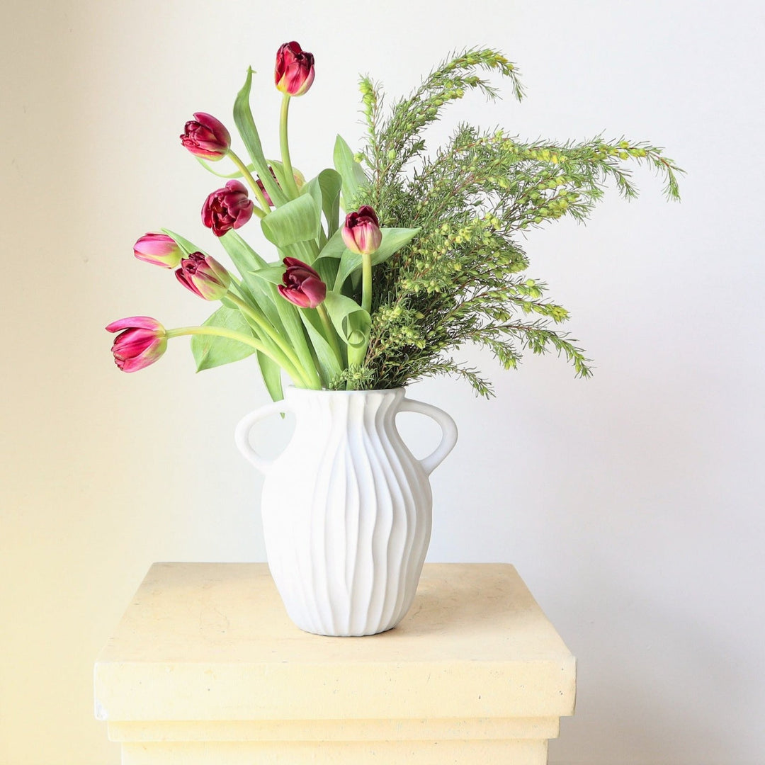 Hand In Hand | A vased arrangement with pink tulips. This arrangement is in a white vase with ribbed sides and a handle on each side.