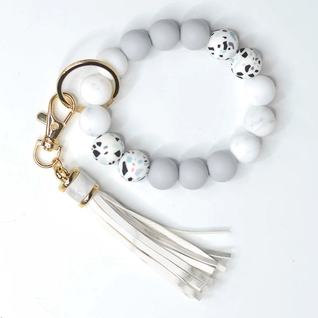 Assorted Beaded Keychains | A gray and speckled keychain bracelet. Accented with a gold keyring and a white tassel. (Some colors may vary with this item).