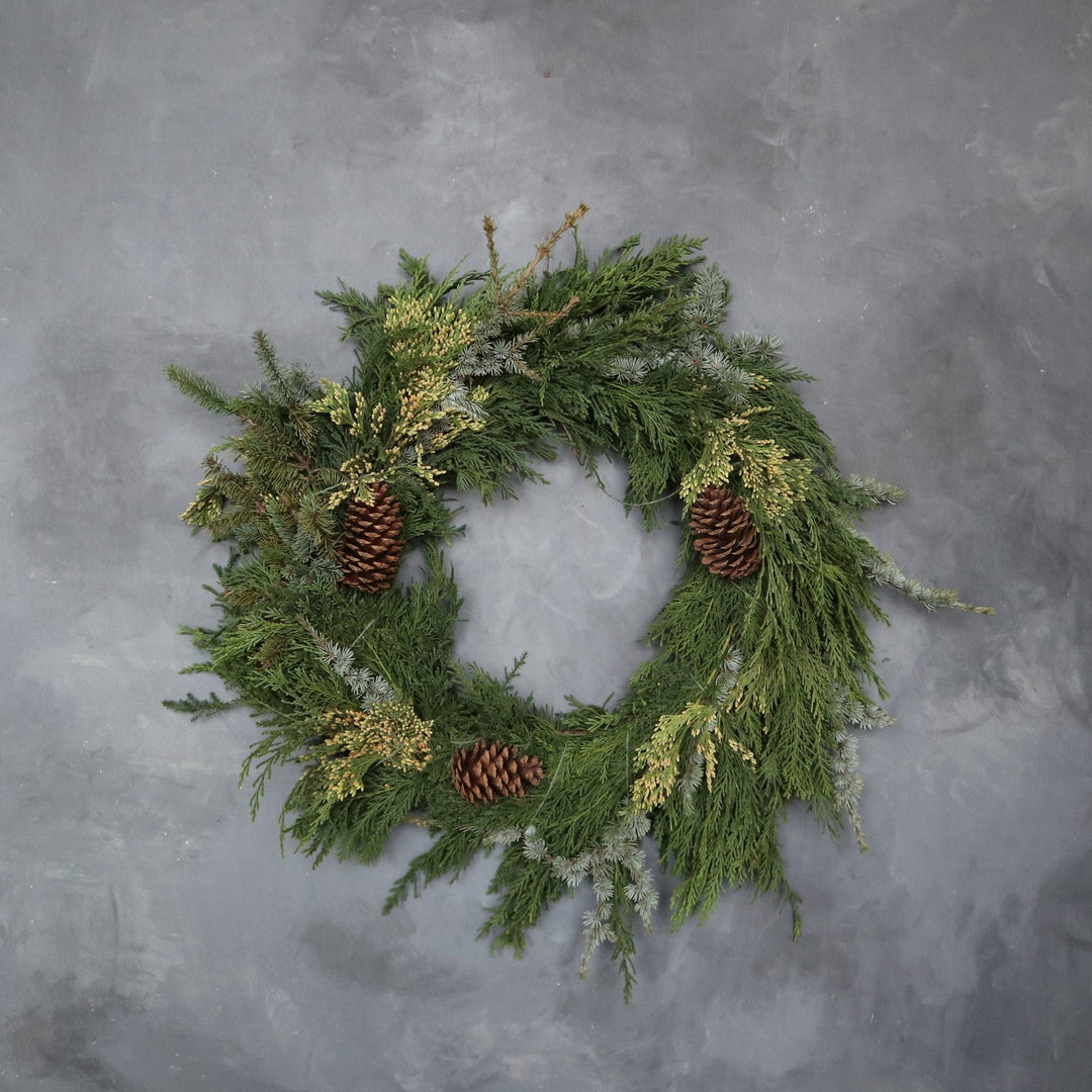 Evergreen wreath with three pinecones taken on mottled gray backdrop.