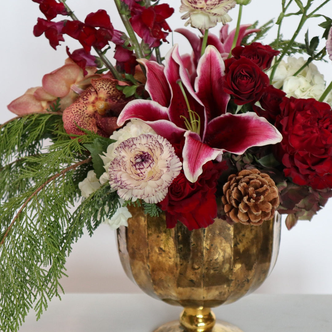 Close up of pink/red/green arrangement in gold vase. Highlights snapdragons, lillies, orchids and other seasonal blooms.